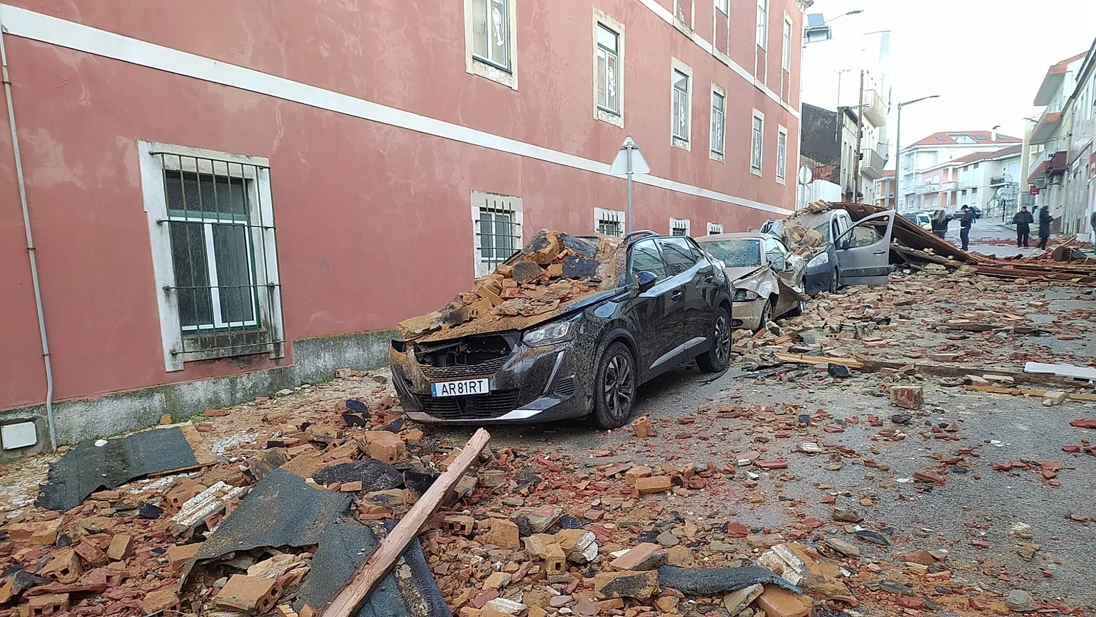 Voiture stationnée dans une rue portugaise lourdement endommagée par des gravats et des morceaux de façade tombés d'un bâtiment lors du passage de la tempête Kristin.