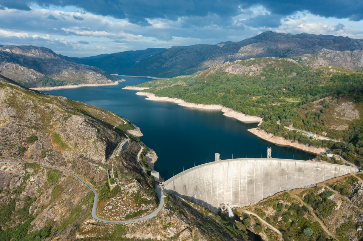 Vue aérienne d'un barrage hydroélectrique massif au Portugal au cœur d'un paysage montagneux avec un réservoir d'eau bleu profond.